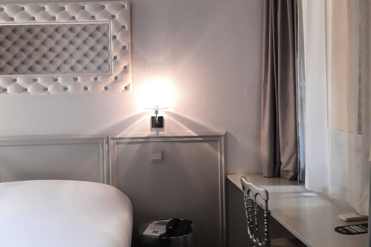 Een hotelkamer met een bed, een bureau, een stoel, een prullenbak en een wandlamp.