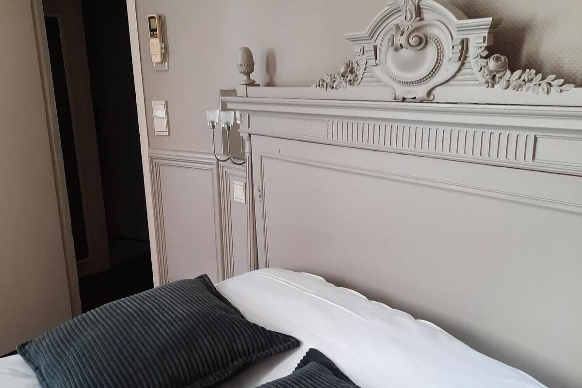 Een opgemaakt bed met een wit hoofdeinde en twee donkere kussens.