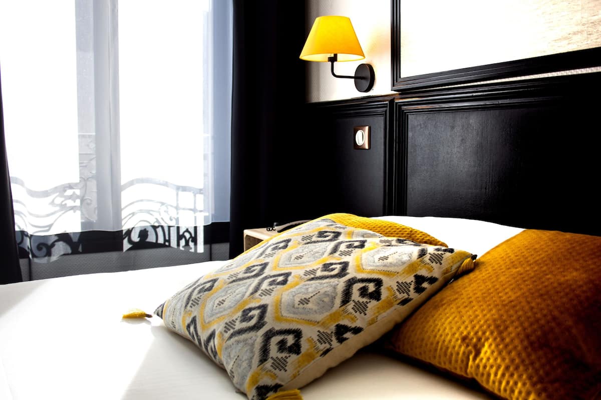 Hotelkamer met een bed, een gekleurd kussen, een gele lamp en uitzicht op een balkon.