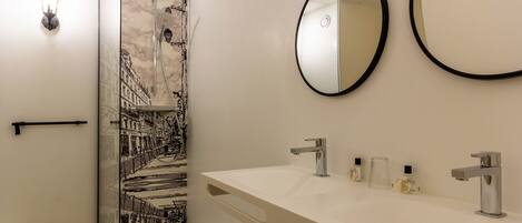 Un baño moderno con tocador blanco, dos espejos redondos, ducha con puerta de cristal y una lámpara de pared.