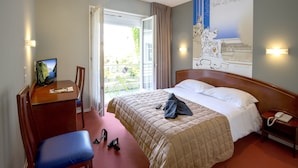 A hotel room with a bed, a desk with a computer, a chair, and a phone on a nightstand.