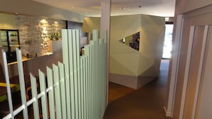 A modern interior with a geometric partition, a stone wall, and a reception area with a counter and plants.