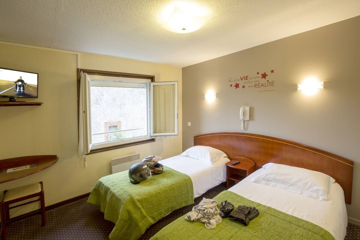 A hotel room with two beds, a desk, a chair, a window, and a wall decoration.
