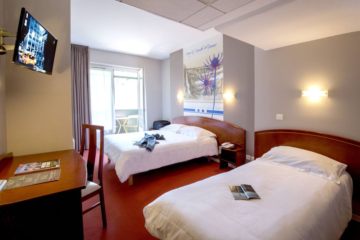 A hotel room with two beds, a desk, a TV, and a window with curtains.