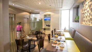 A modern dining area with tables and chairs, a television mounted on the wall, and a stone accent wall.