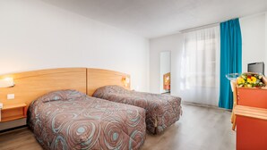 Hotellihuone, jossa on kaksi sänkyä, puinen pääty, työpöytä tuolilla, televisio ja ikkuna, jossa on verhot.