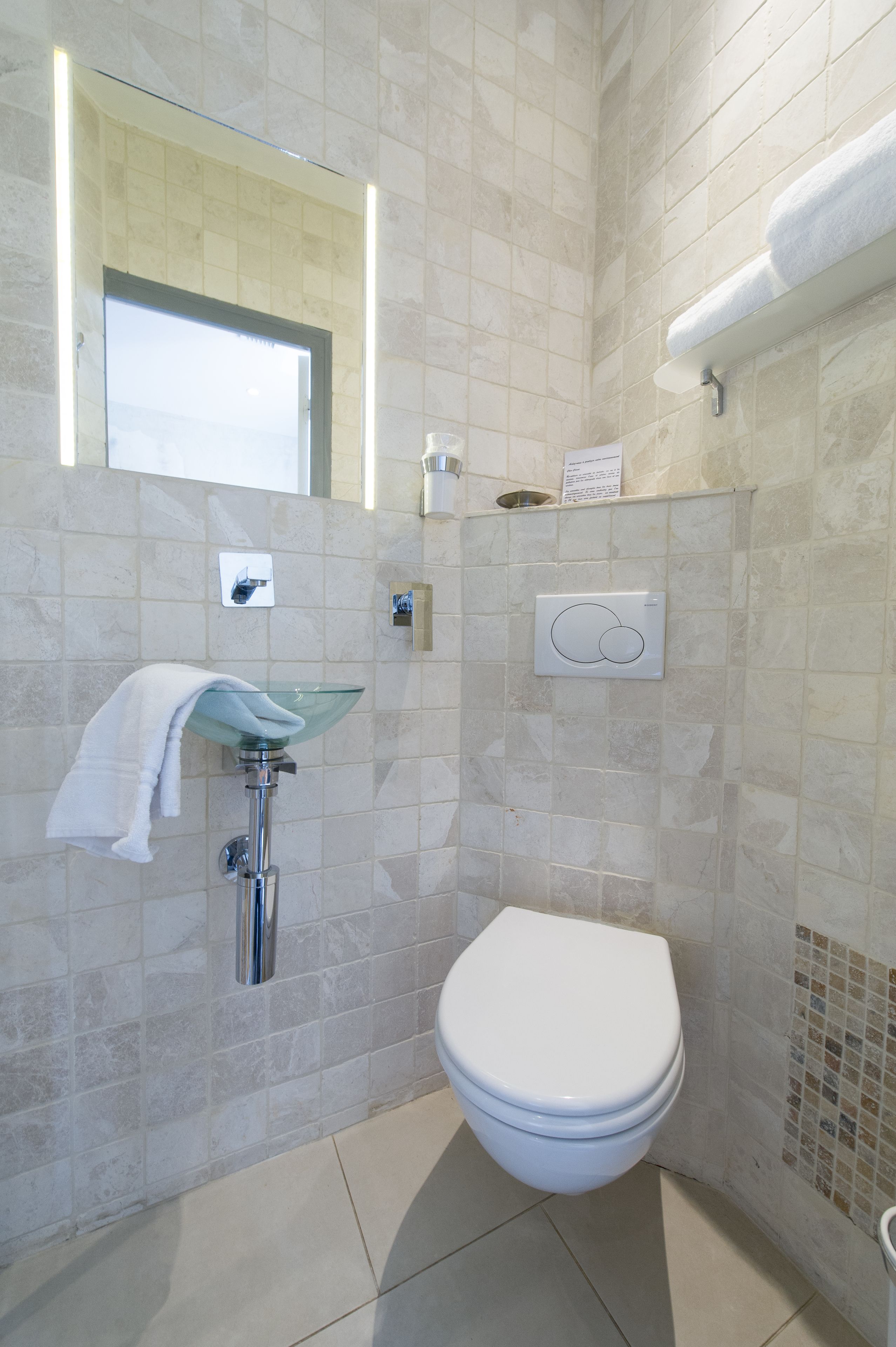 A modern bathroom with a glass sink, a white toilet, and a towel rack.