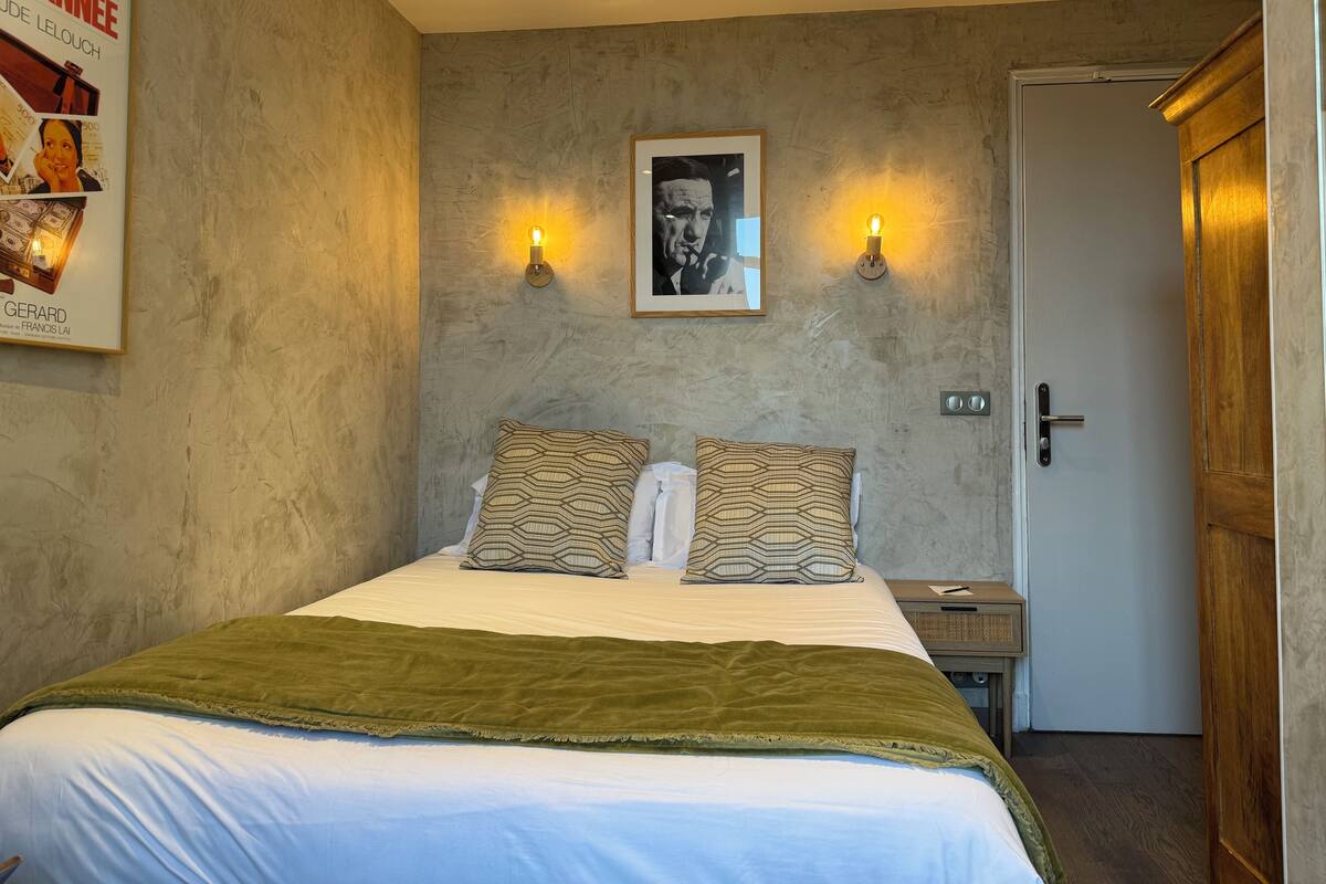 A bedroom with a bed, two bedside tables, a door, and a poster on the wall.