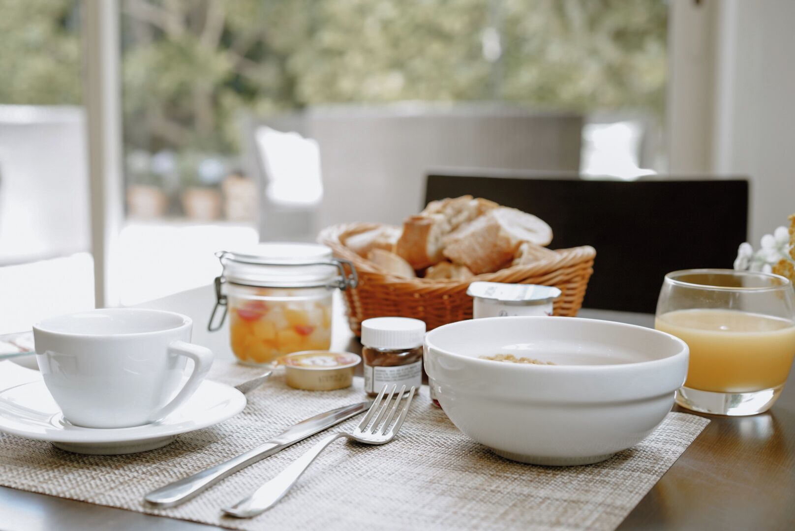 Une table mise pour le petit-déjeuner, avec une tasse, un bol, un pot et un panier de pain.