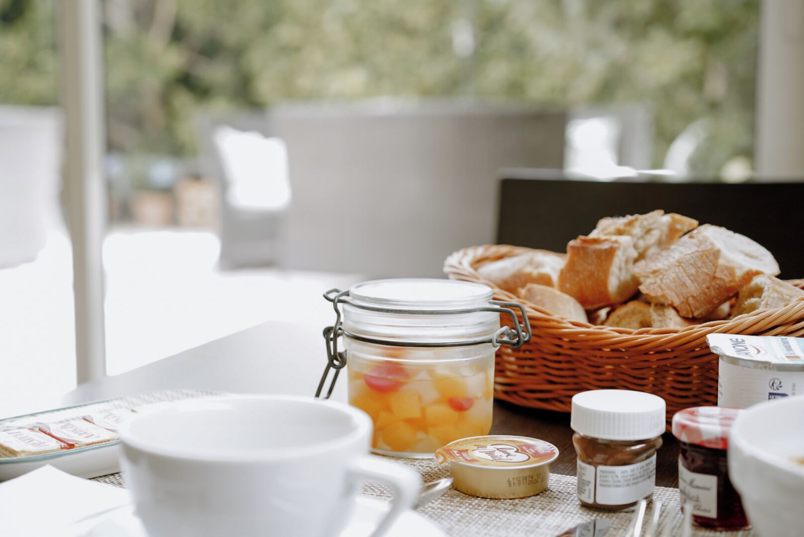 A breakfast setting with a jar of fruit compote, a basket of croissants, and various condiments.
