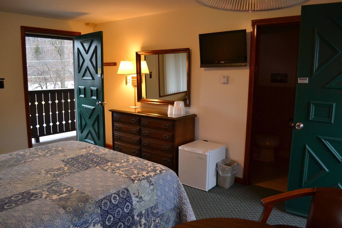 A hotel room with a bed, dresser, mirror, television, and a small refrigerator.