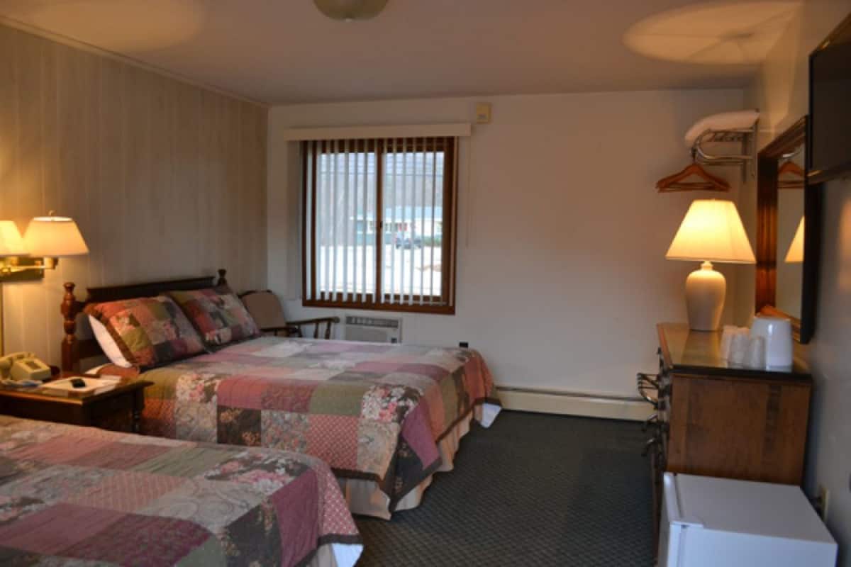 A hotel room with two beds, a desk with a lamp, a dresser, and a window with blinds.
