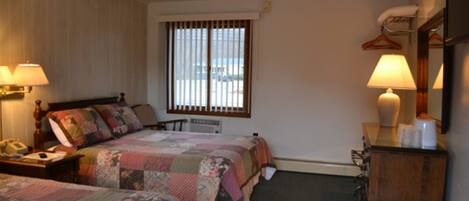 A hotel room with two beds, a desk with a lamp, a dresser, and a window with blinds.