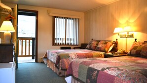 Ein Hotelzimmer mit zwei Betten, einem Schreibtisch, einem Stuhl, einer Lampe, einem Telefon und einem Fenster mit Jalousien.