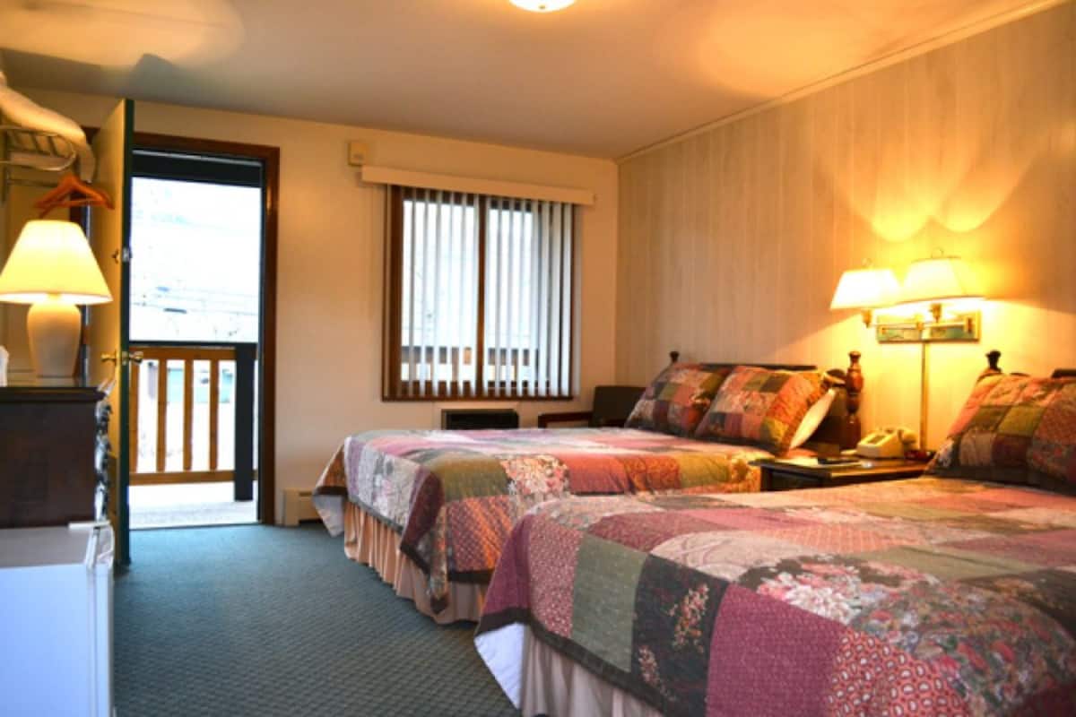 A hotel room with two beds, a desk, a chair, a lamp, a telephone, and a window with blinds.