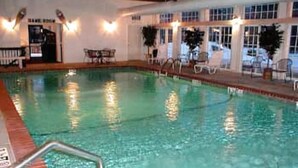 Ein Schwimmbecken mit glatter Wasseroberfläche, umgeben von einer gefliesten Liegefläche und einem Holzdeck.