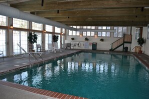 Piscina interna con acqua cristallina, circondata da sedie a sdraio e una scala.