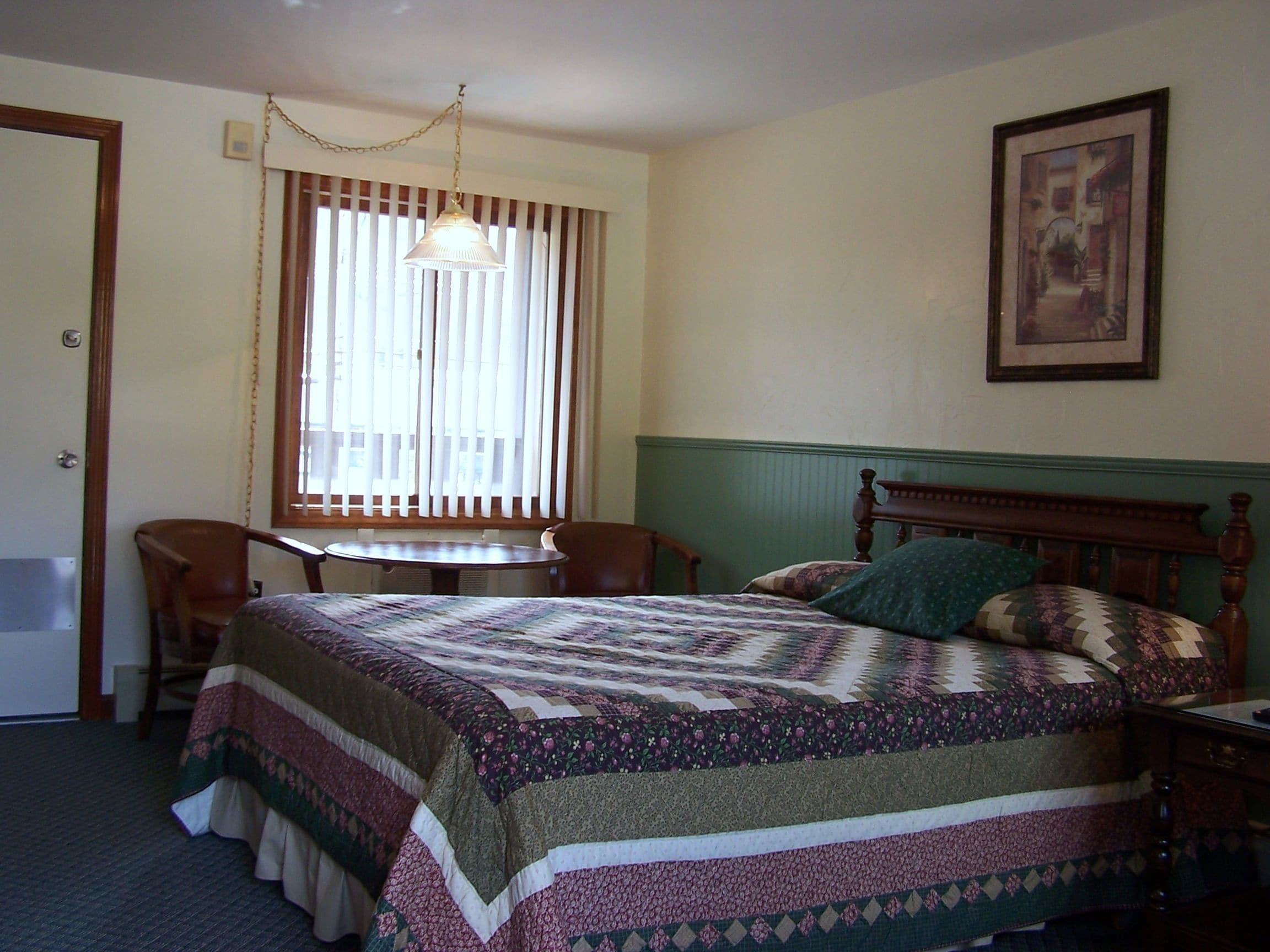 A room with a bed, a chair, a table, and a window with blinds.