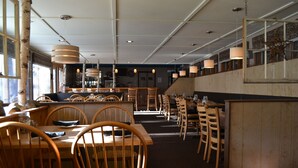 Ein Restaurant mit Holztischen und -stühlen, einer Bar und Pendelleuchten.