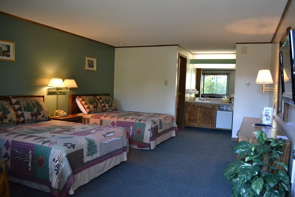 A room with two beds, a small kitchenette, and a bathroom.