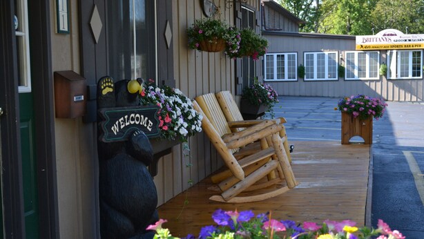 Eine Holzterrasse mit einem Schaukelstuhl und einem Willkommensschild, umgeben von Blumentöpfen und Blumen.