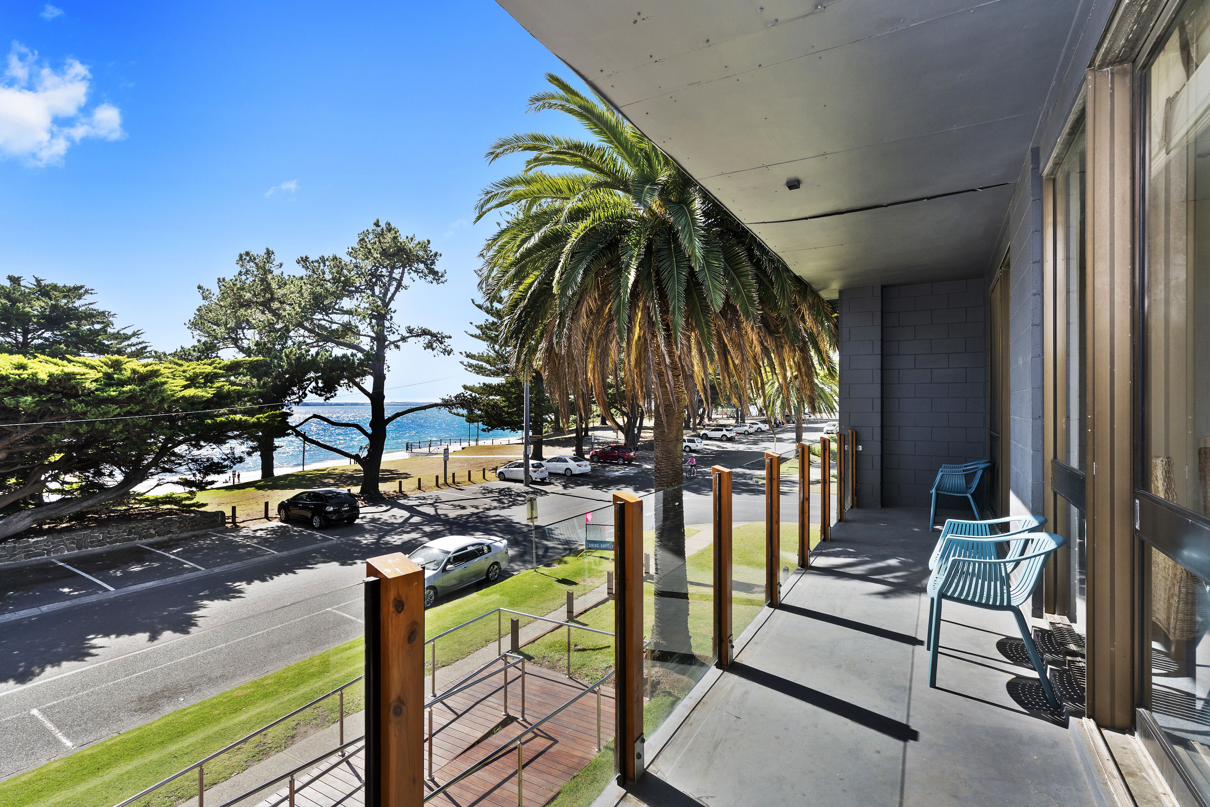 A balcony with a view of the street, parked cars, and a palm tree.