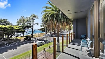 A balcony with a view of the street, parked cars, and a palm tree.
