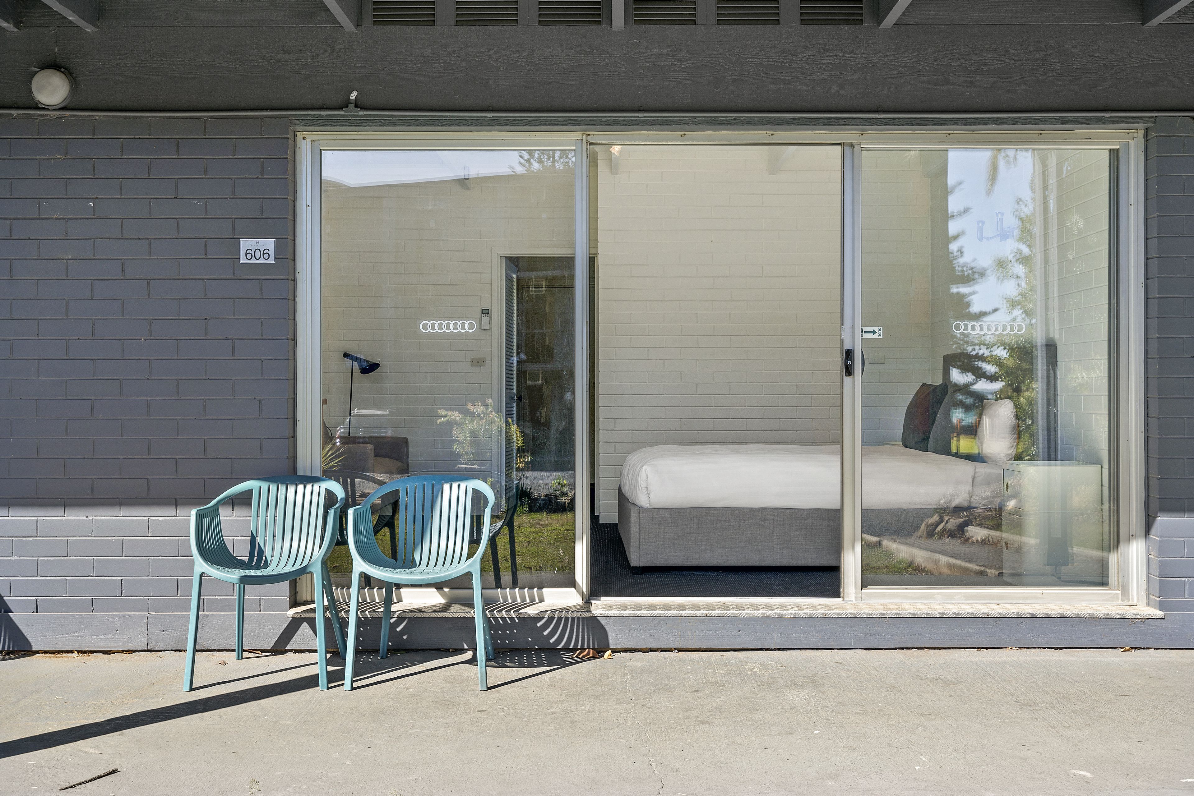 Une porte-fenêtre coulissante donne accès à une chambre à coucher qui comprend un lit et une chaise placée à l’extérieur.