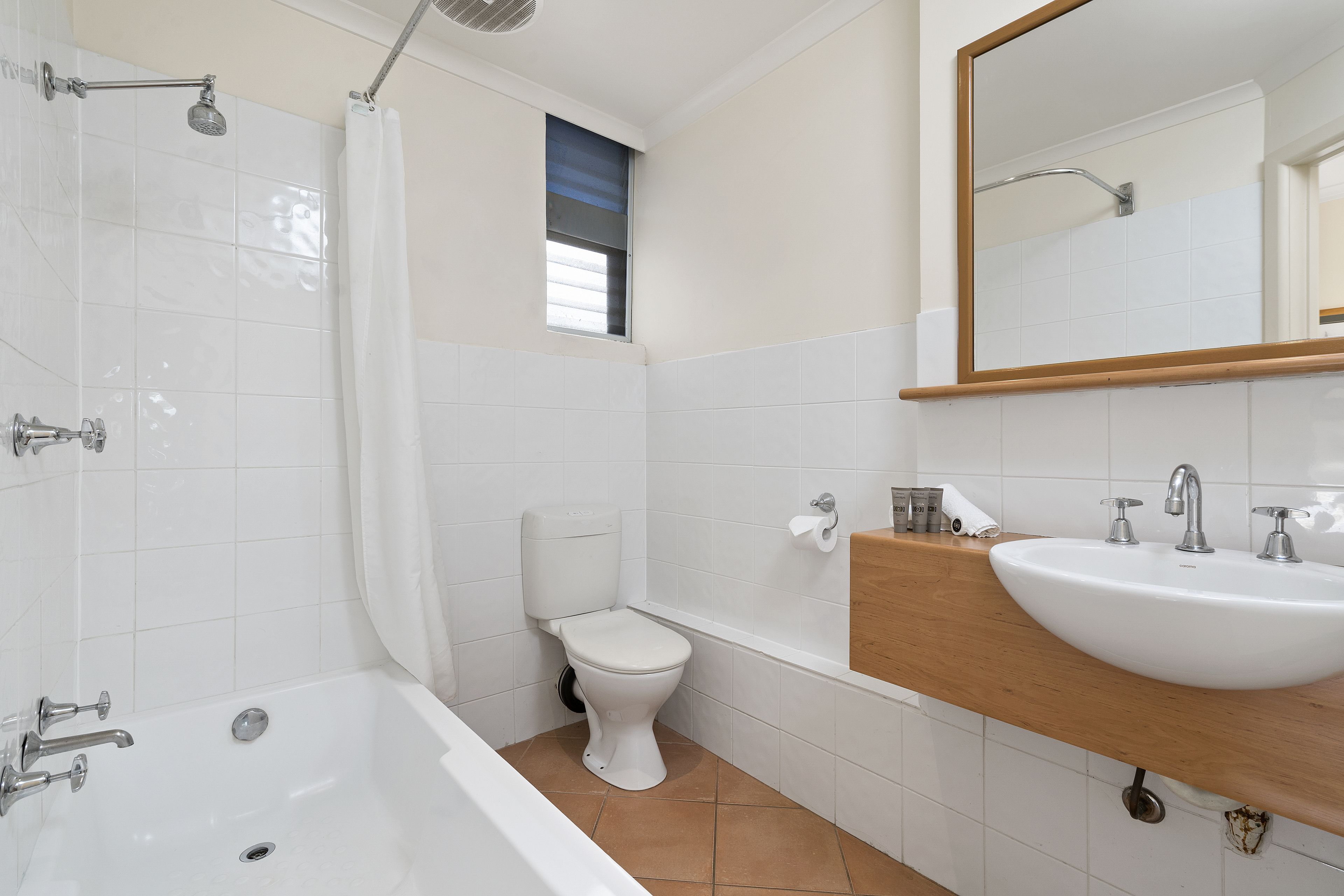 Ein Badezimmer mit einer weißen Badewanne, einer Toilette und einem Waschbecken mit Holzablagefläche.