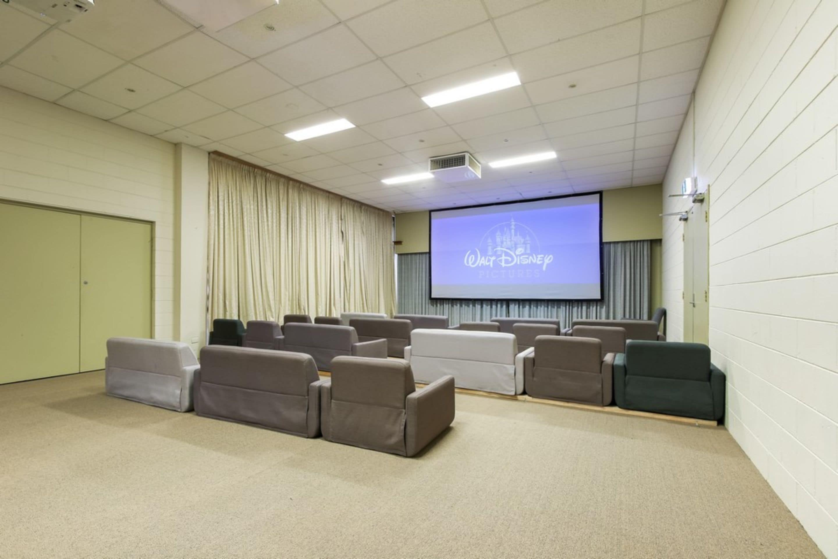 A movie theater with rows of seats, a screen displaying the Walt Disney Pictures logo, and a projector.
