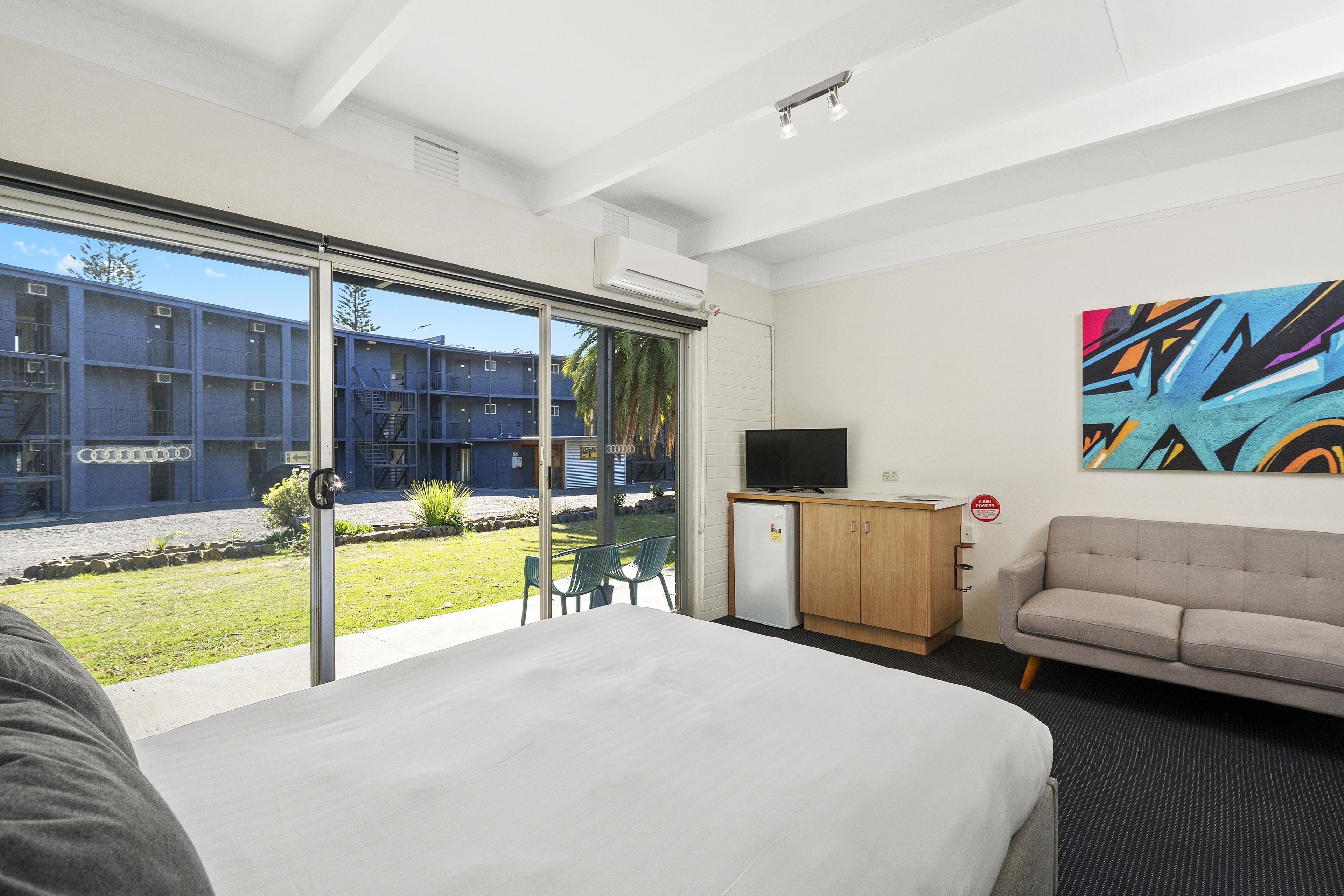 Quarto de hotel com uma cama grande, televisão, sofá e uma porta de vidro deslizante que dá para um pátio.