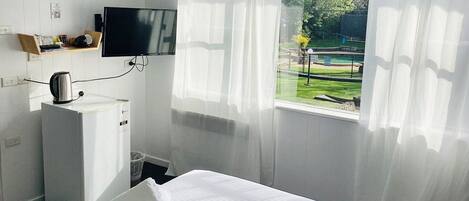 A hotel room with a bed, a television mounted on the wall, a kettle, and a window with sheer curtains.
