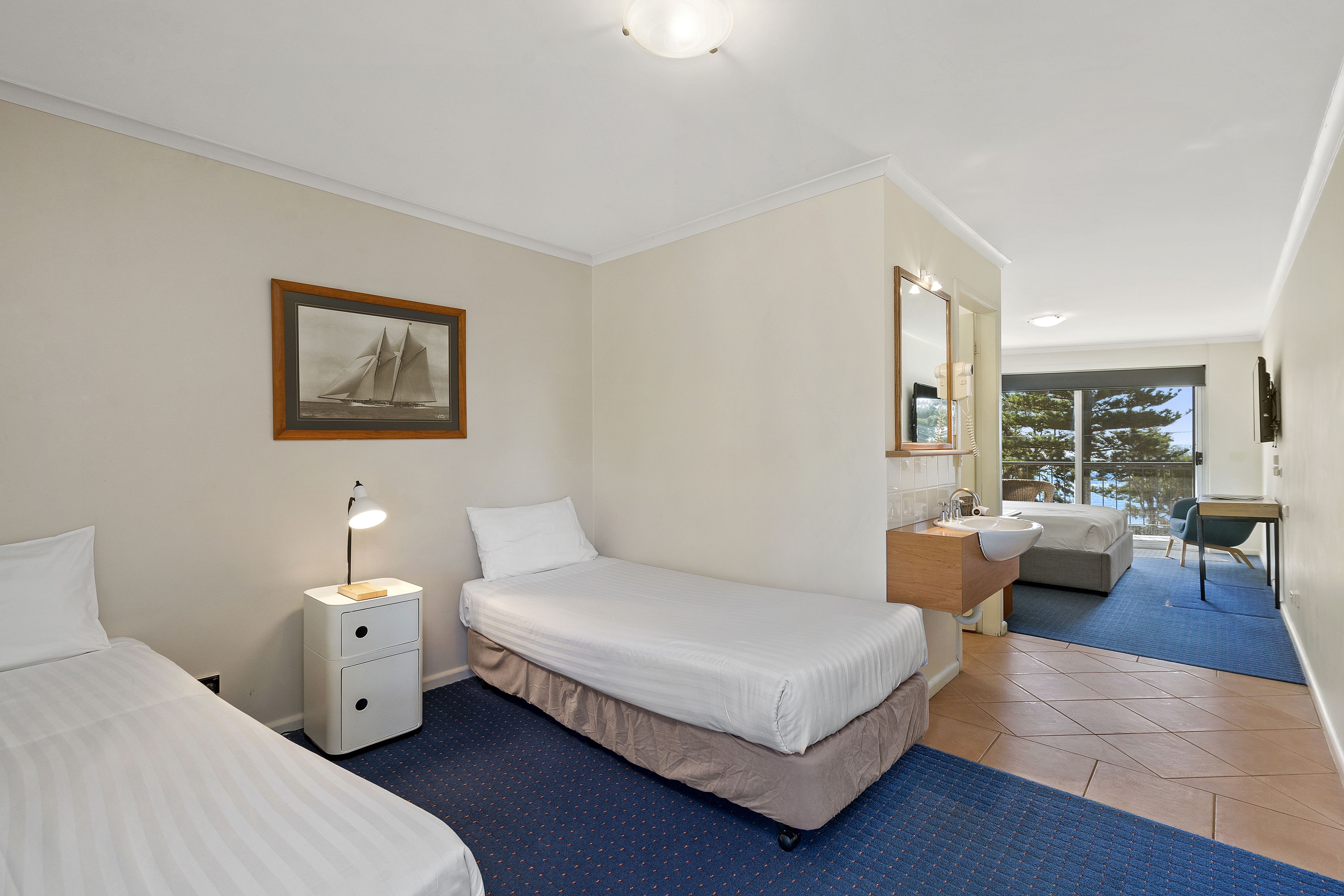 A hotel room with a bed, a nightstand with a lamp, a bathroom with a sink, and a view of the outdoors.