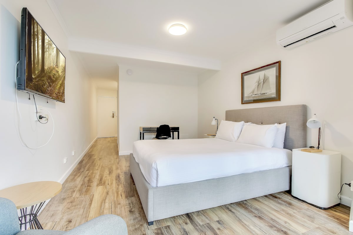 Moderni hotellihuone, jossa on suuri sänky, työpöytä, tuoli ja seinälle asennettu televisio.