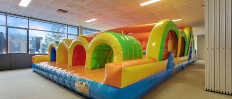 A large inflatable play area with multiple arches and a padded floor, located indoors with a view of buildings outside.