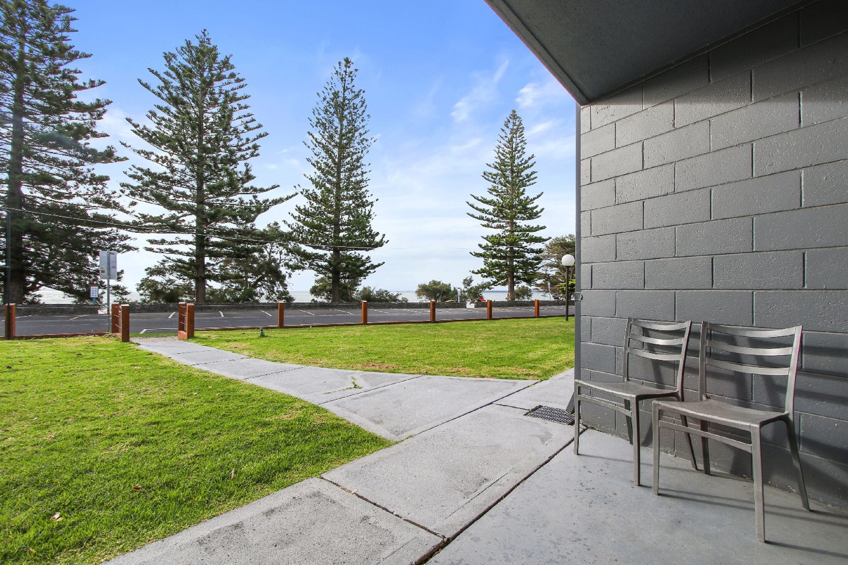 An outdoor seating area with two metal benches, a concrete pathway, and a grassy lawn.