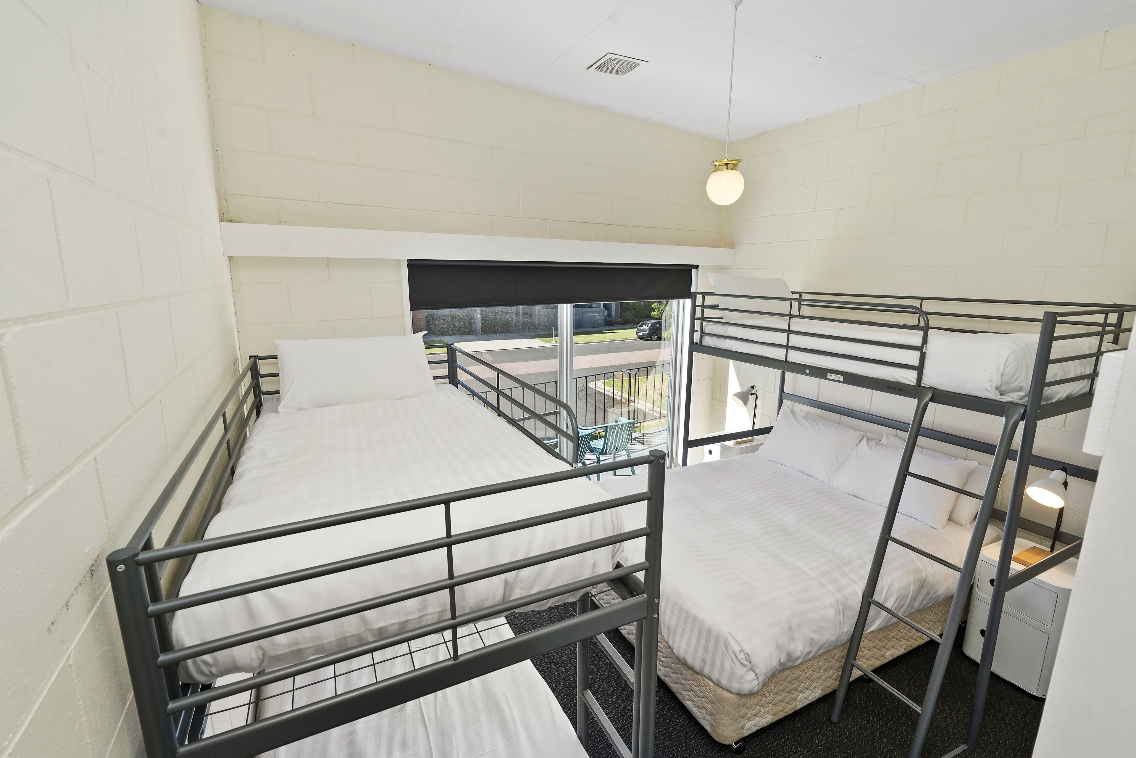 A dormitory room with bunk beds, a window with a view, and a small table with a chair.