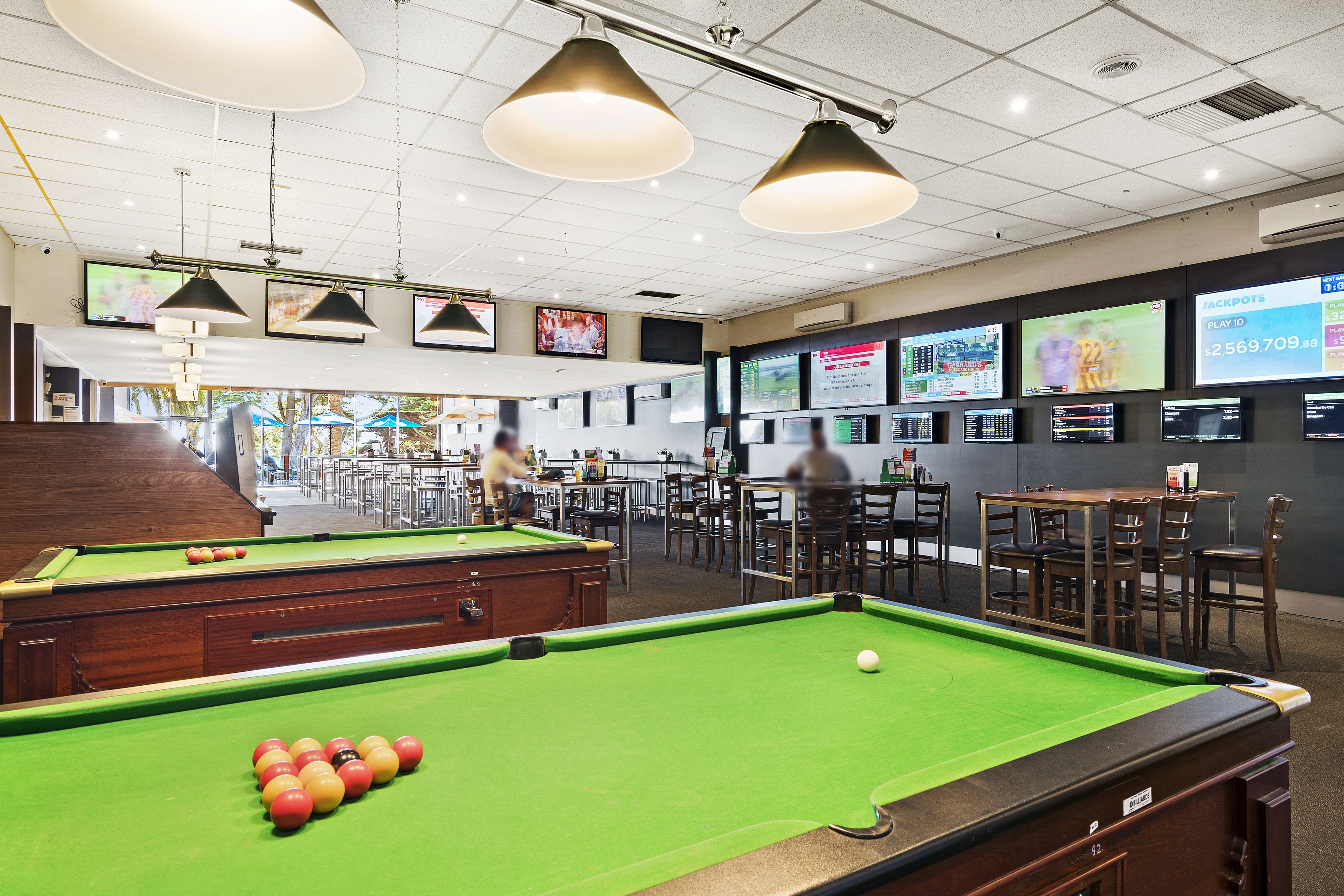 Una sala de billar con varias mesas y una mesa de billar, una zona de bar y un área de estar con mesas y sillas.