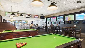 Una sala de billar con varias mesas y una mesa de billar, una zona de bar y un área de estar con mesas y sillas.