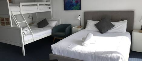 Una habitación de hotel con literas, una cama individual, una silla, un escritorio y un cuadro en la pared.
