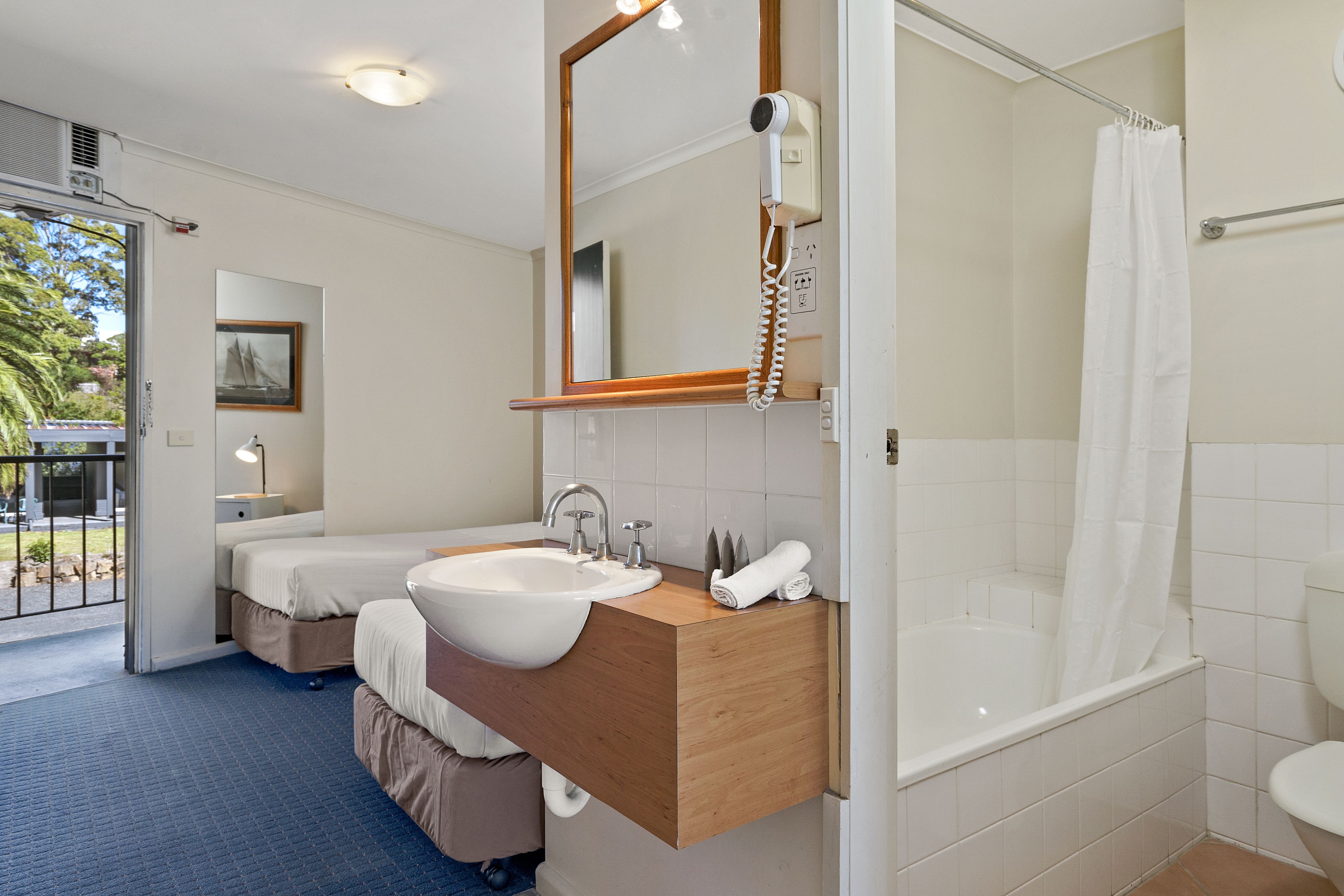 A modern bathroom with a double sink, a large mirror, a hairdryer, and a bathtub.