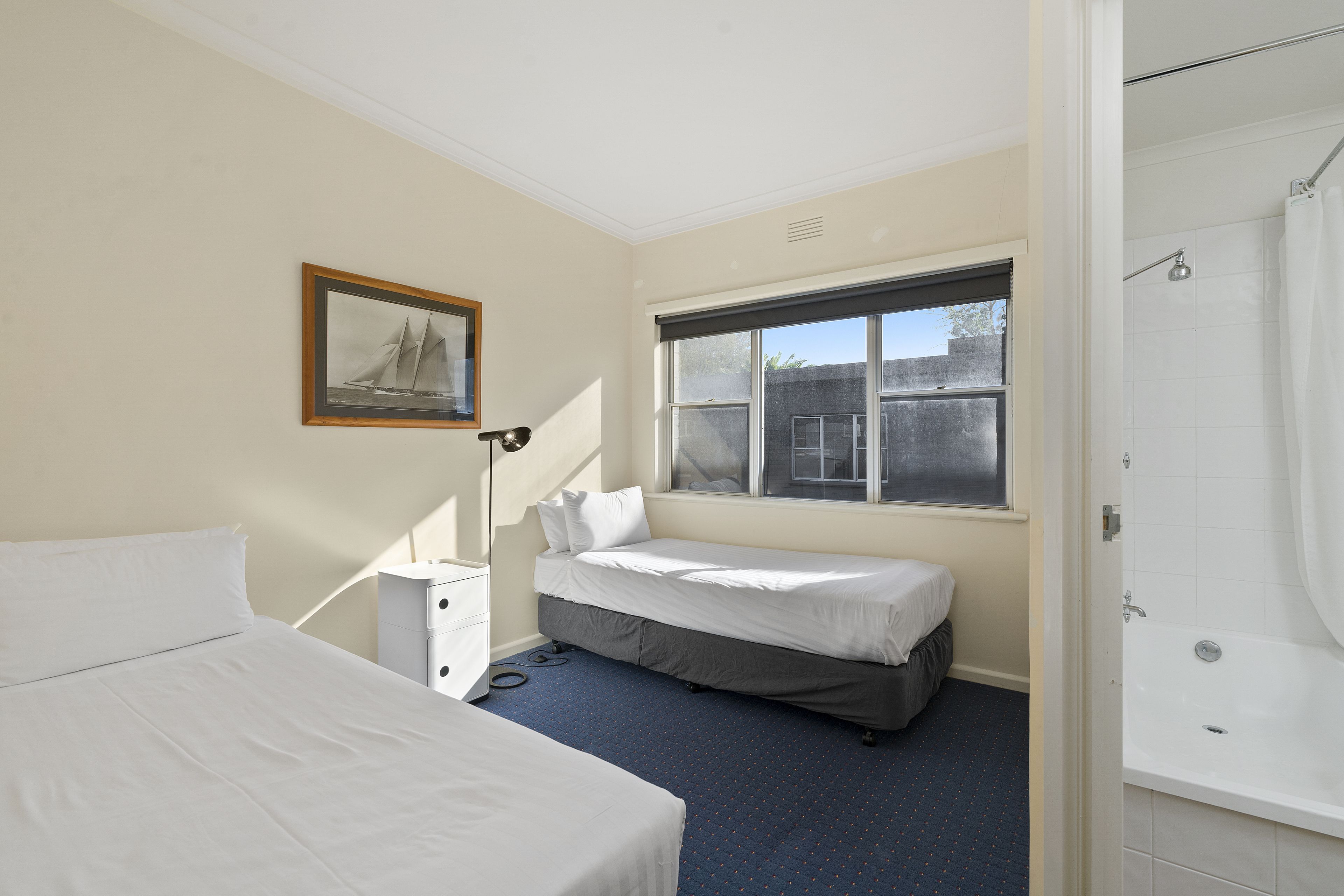 A bedroom with a bed, a small bedside table, a window with a view, and a bathroom with a shower.