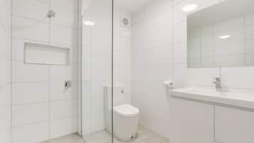 A modern bathroom with white tiles, a glass shower enclosure, a toilet, and a sink with a mirror.