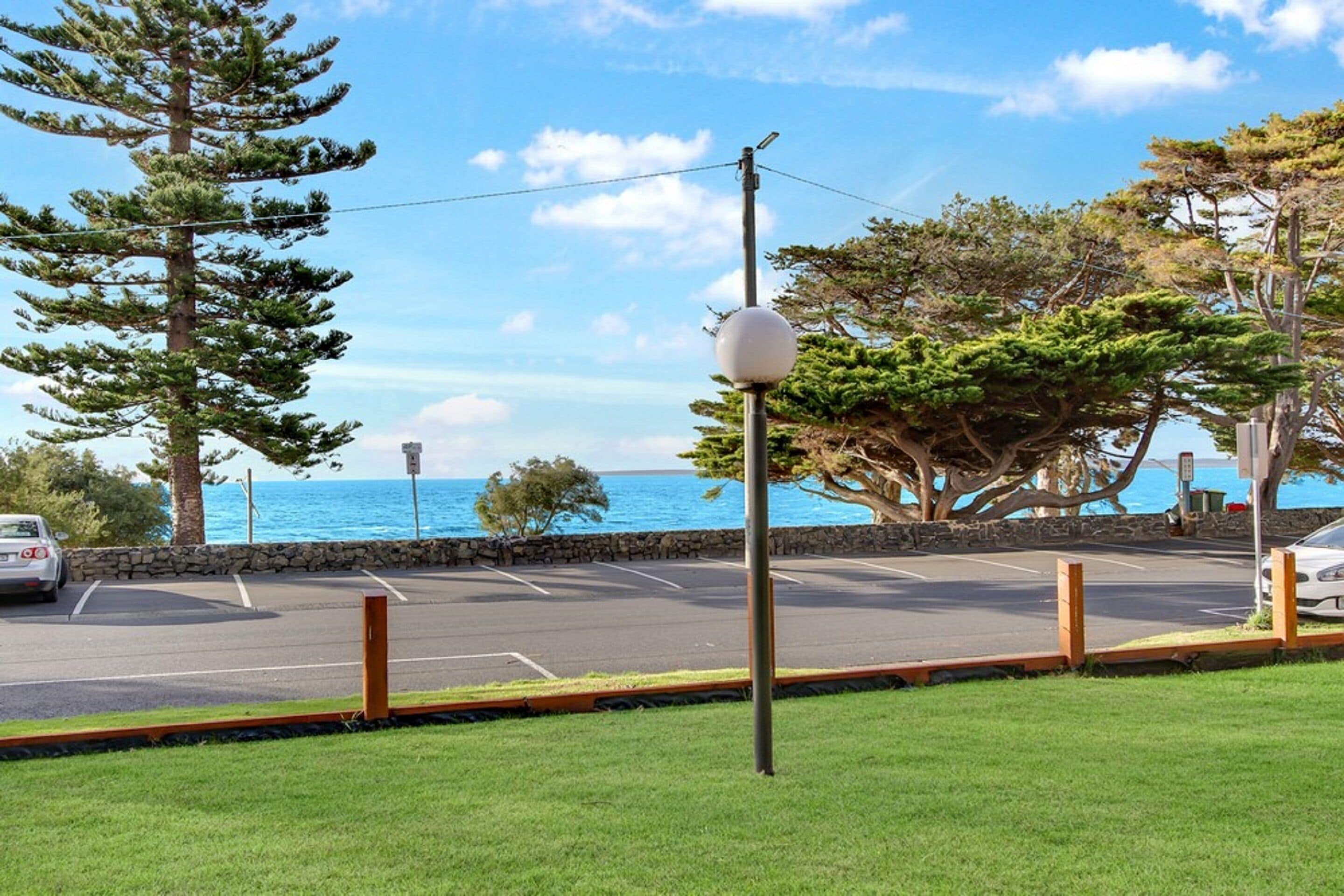 Un estacionamiento con vista al océano, una farola y un árbol.