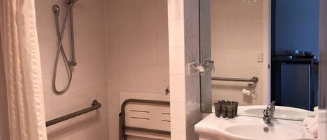 Un baño con ducha, lavamanos y espejo.