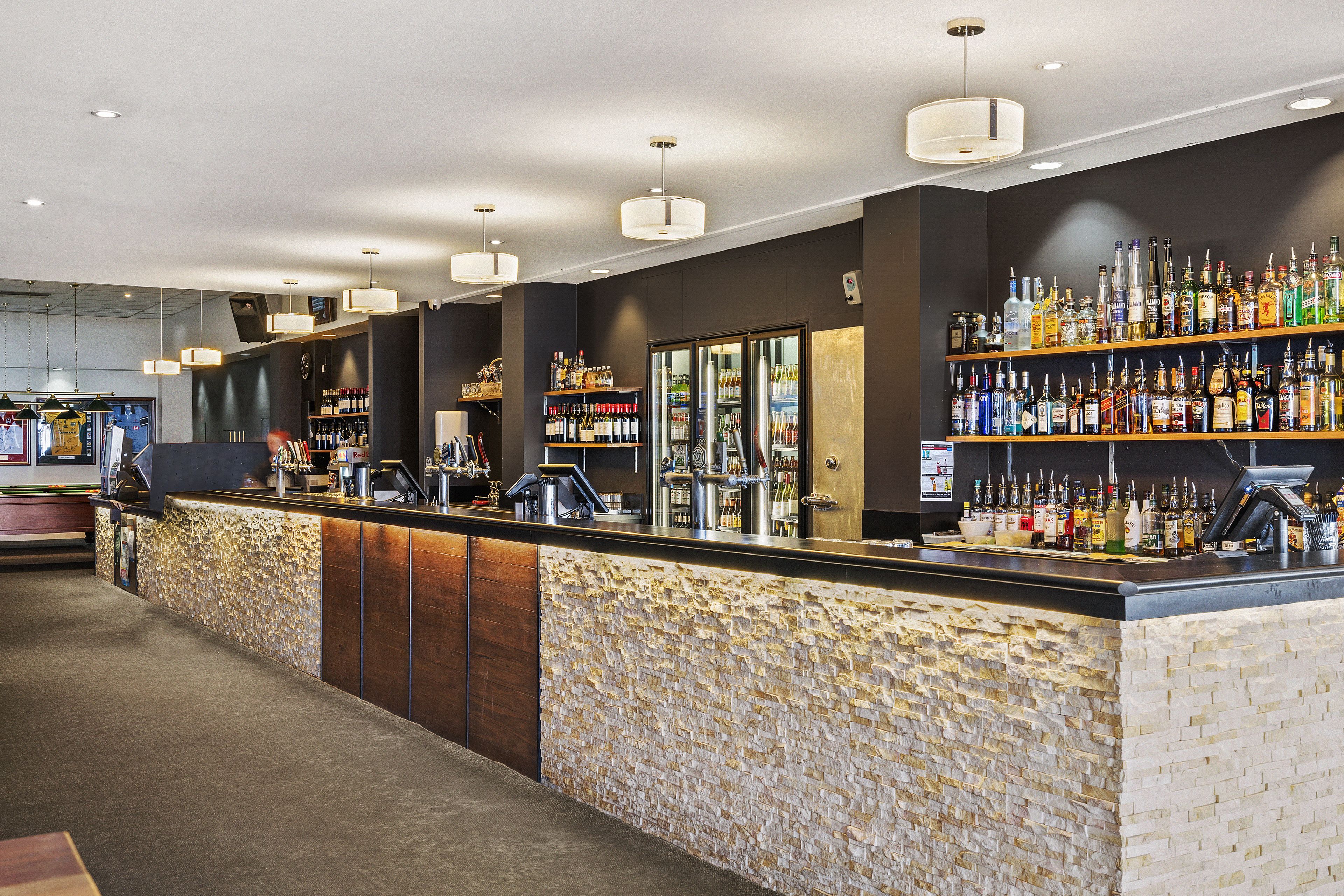 A bar area with a stone-textured counter, shelves of liquor bottles, and pendant lighting.