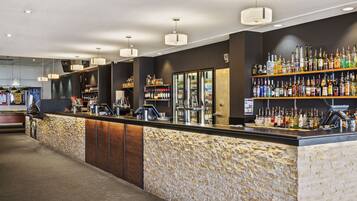 A bar area with a stone-textured counter, shelves of liquor bottles, and pendant lighting.