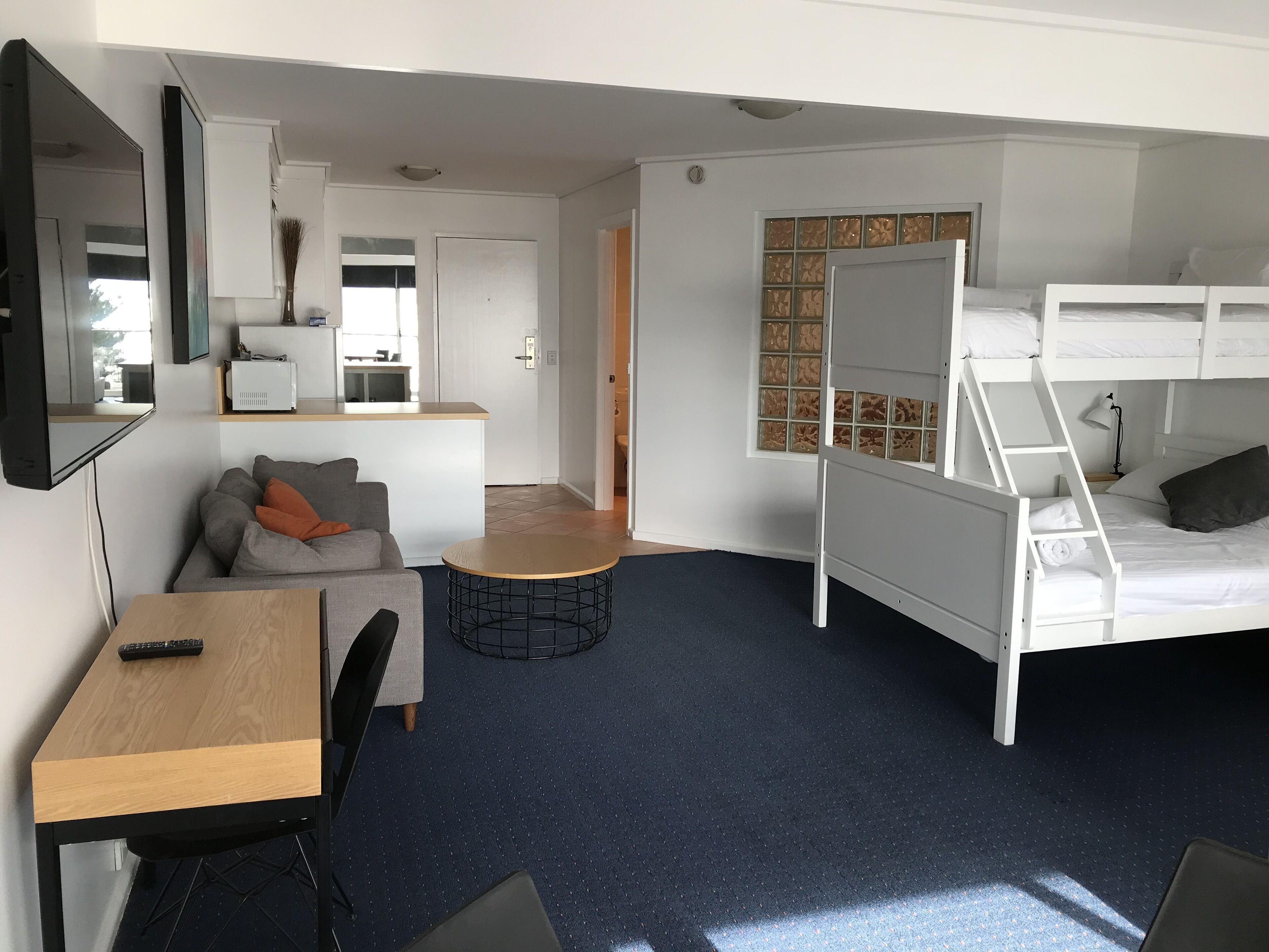 Et lille værelse med køjeseng, skrivebord med stol, lille rundt bord og sofa.