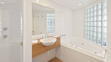 Une salle de bain moderne avec une grande baignoire, un meuble-lavabo en bois, un lavabo blanc et une fenêtre en blocs de verre.