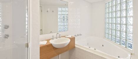 Un baño moderno con una bañera grande, un tocador de madera, un lavabo blanco y una ventana de bloques de vidrio.